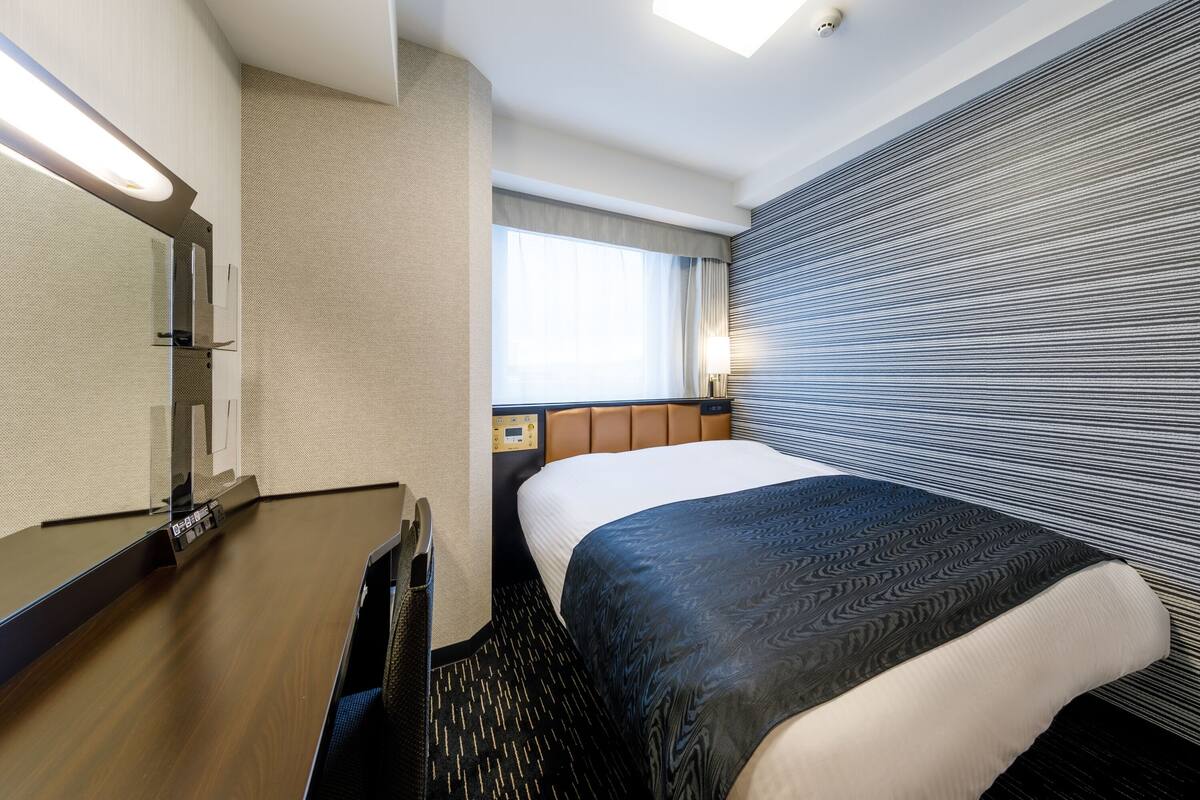 Hotellihuone, jossa on suuri sänky, yöpöytä, peili ja ikkuna, jossa on verhot.