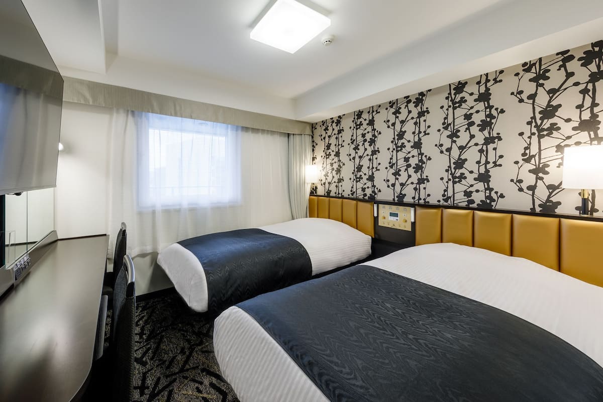 Hotellihuone, jossa on kaksi sänkyä, työpöytä, televisio ja ikkuna, jossa on verhot.
