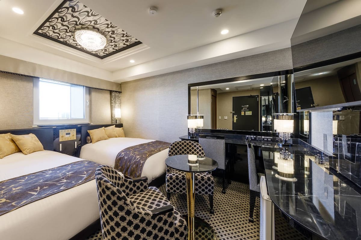 Hotellihuone, jossa on kaksi sänkyä, työpöytä, tuoli, peili ja kylpyhuone.