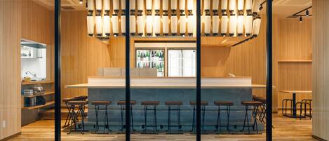 A modern bar area with a wooden interior, a glass partition, and a row of bar stools.