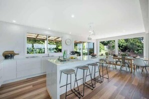 A modern kitchen with a central island, bar stools, and large windows offering a view of greenery.