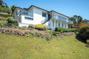 A modern two-story house with a stone retaining wall, large windows, and a balcony.