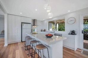 A modern kitchen with a central island, bar stools, a built-in oven, and a large window providing natural light. - House on the Hill with a View – Sleeps 12, 3 Bath. (Sandy Bay)