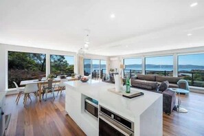 A modern kitchen with a central island, dining area with chairs, and a sofa with a view. - House on the Hill with a View – Sleeps 12, 3 Bath. (Sandy Bay)