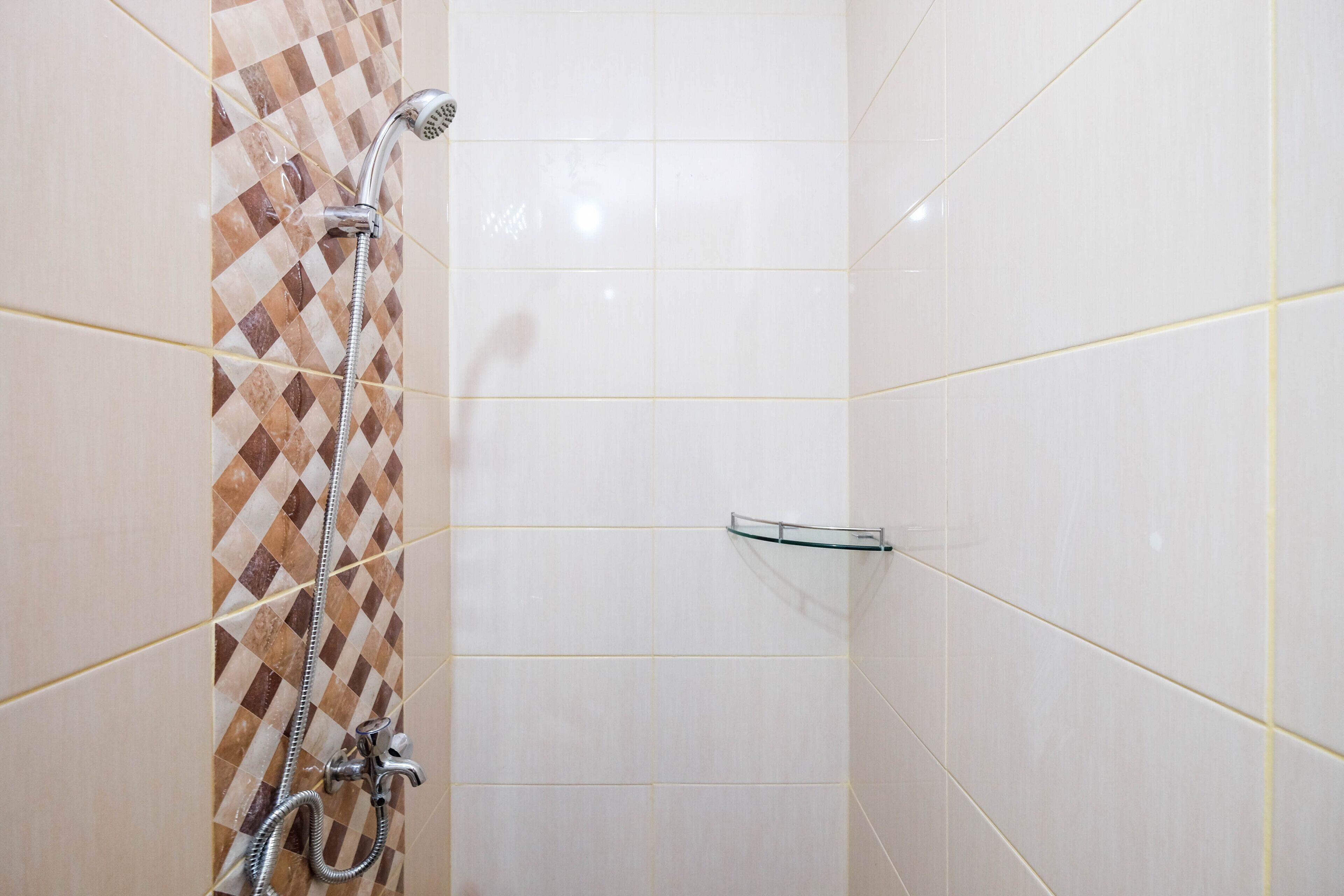 A shower area with a tiled wall, a showerhead, and a glass shelf.