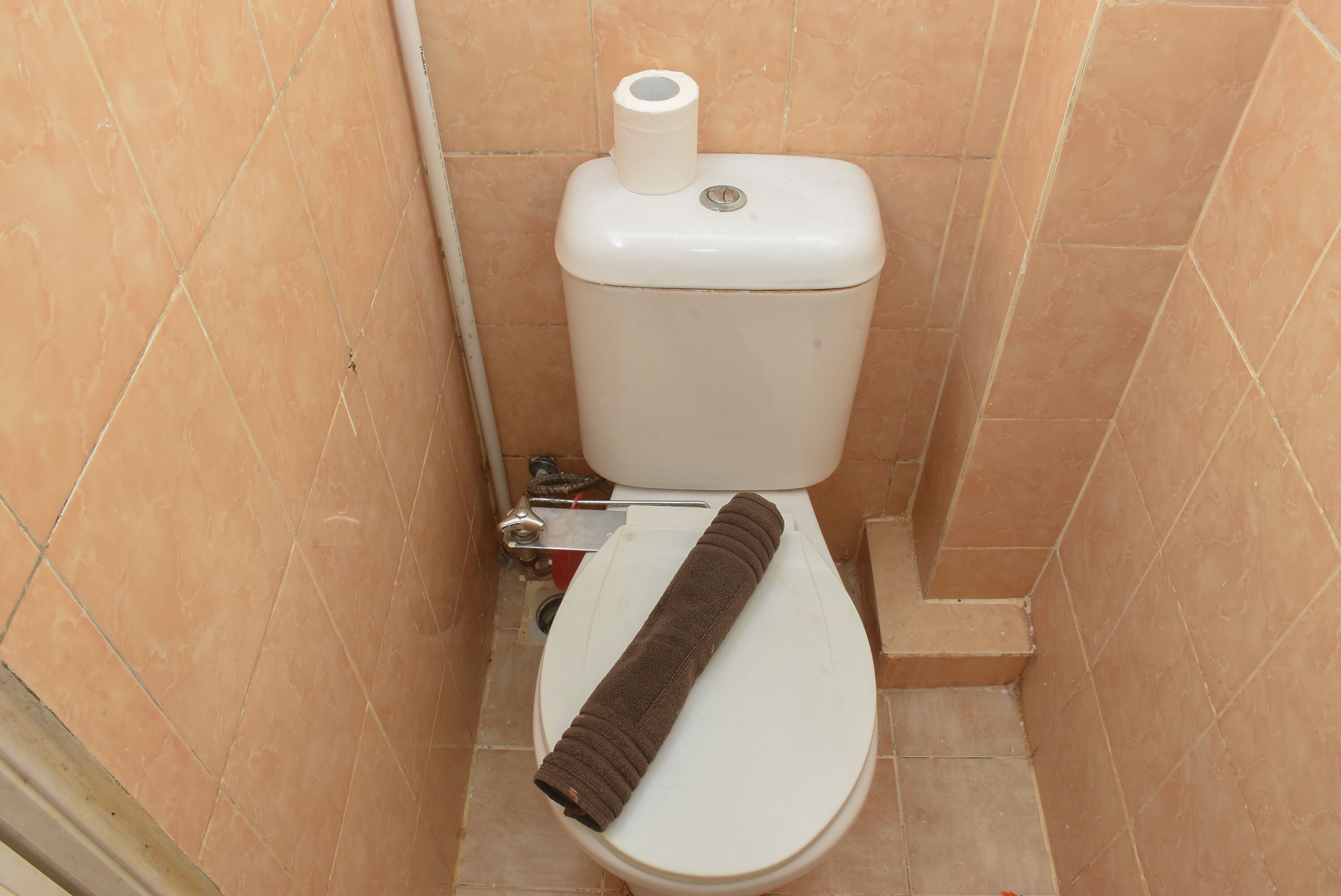 A toilet with a towel on the seat and a toilet paper roll on the tank.
