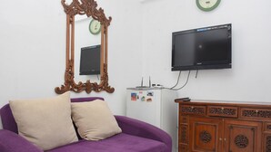 Un sofá púrpura con dos almohadas, un aparador de madera con intrincados grabados, un refrigerador blanco y un televisor de pantalla plana montado en la pared.