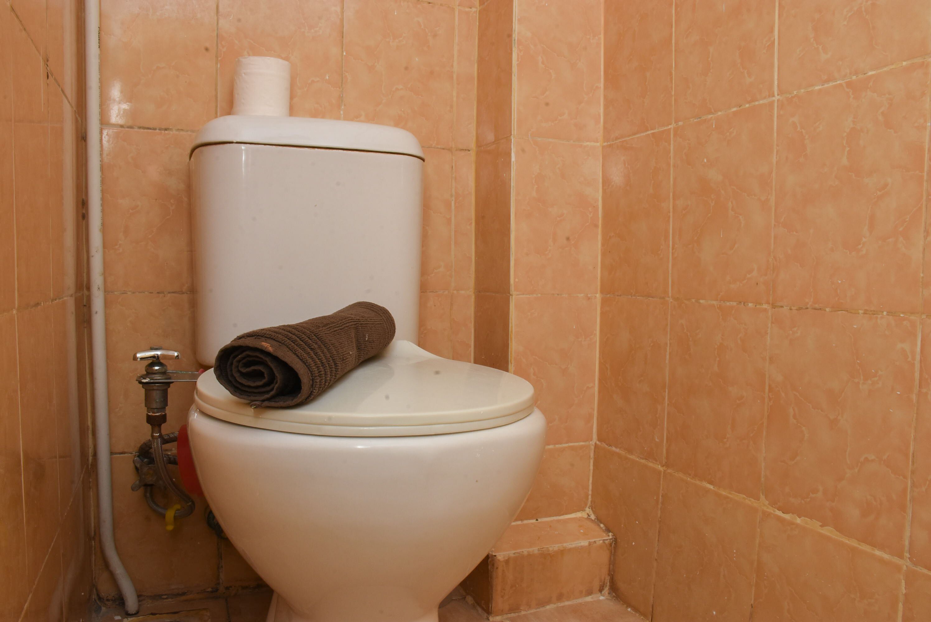 Des toilettes avec une serviette sur le siège, un porte-rouleau de papier toilette et un tuyau sur le côté gauche.