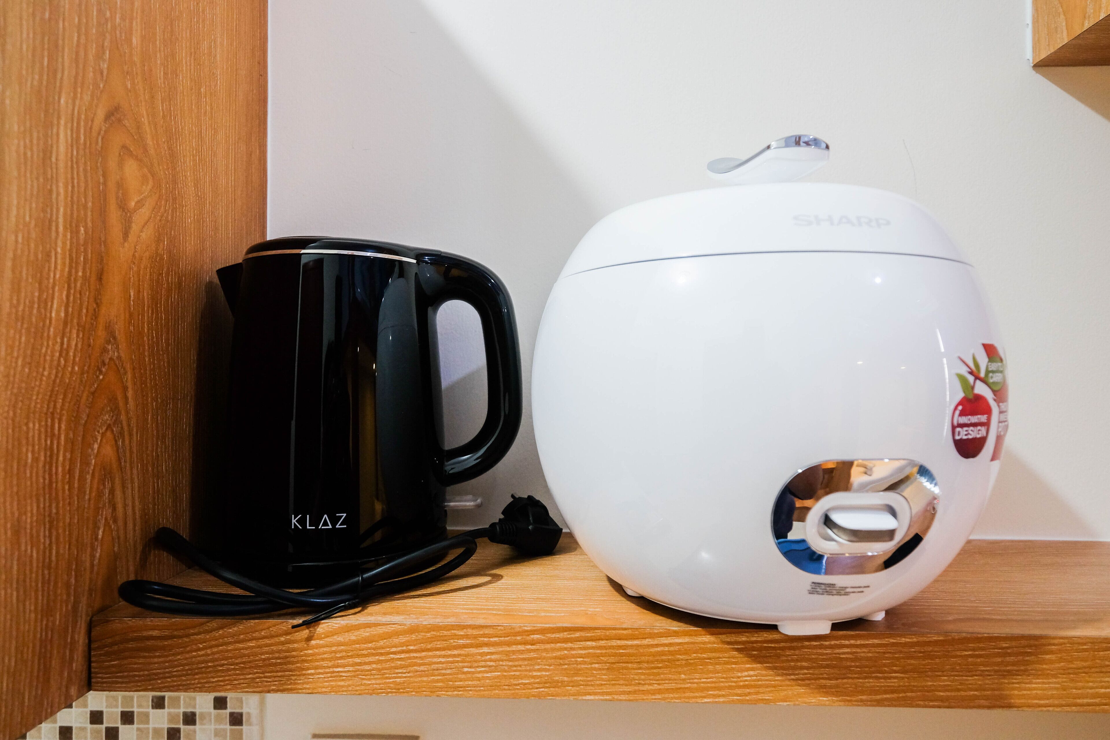 Una cafetera negra y una tetera eléctrica blanca sobre un estante de madera.