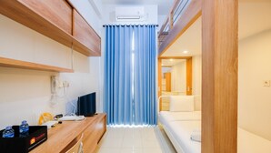 Een kleine hotelkamer met een houten bureau, een bed en een badkamer achter een gordijn.