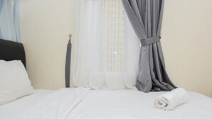 Une chambre d’hôtel avec un lit, du linge de lit blanc, une fenêtre avec des rideaux légers et un rideau gris maintenu en retrait.