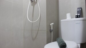 A modern bathroom with a toilet, a shower, and a towel on the seat. - Pleasurable Studio Room Near Unpad At Taman Melati Jatinangor Apartment (Hegarmanah)