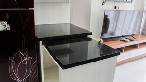 A kitchen with a black countertop, a refrigerator, a microwave, and a wooden TV stand. - Comfort 1Br At Casa De Parco Apartment (Pagedangan)
