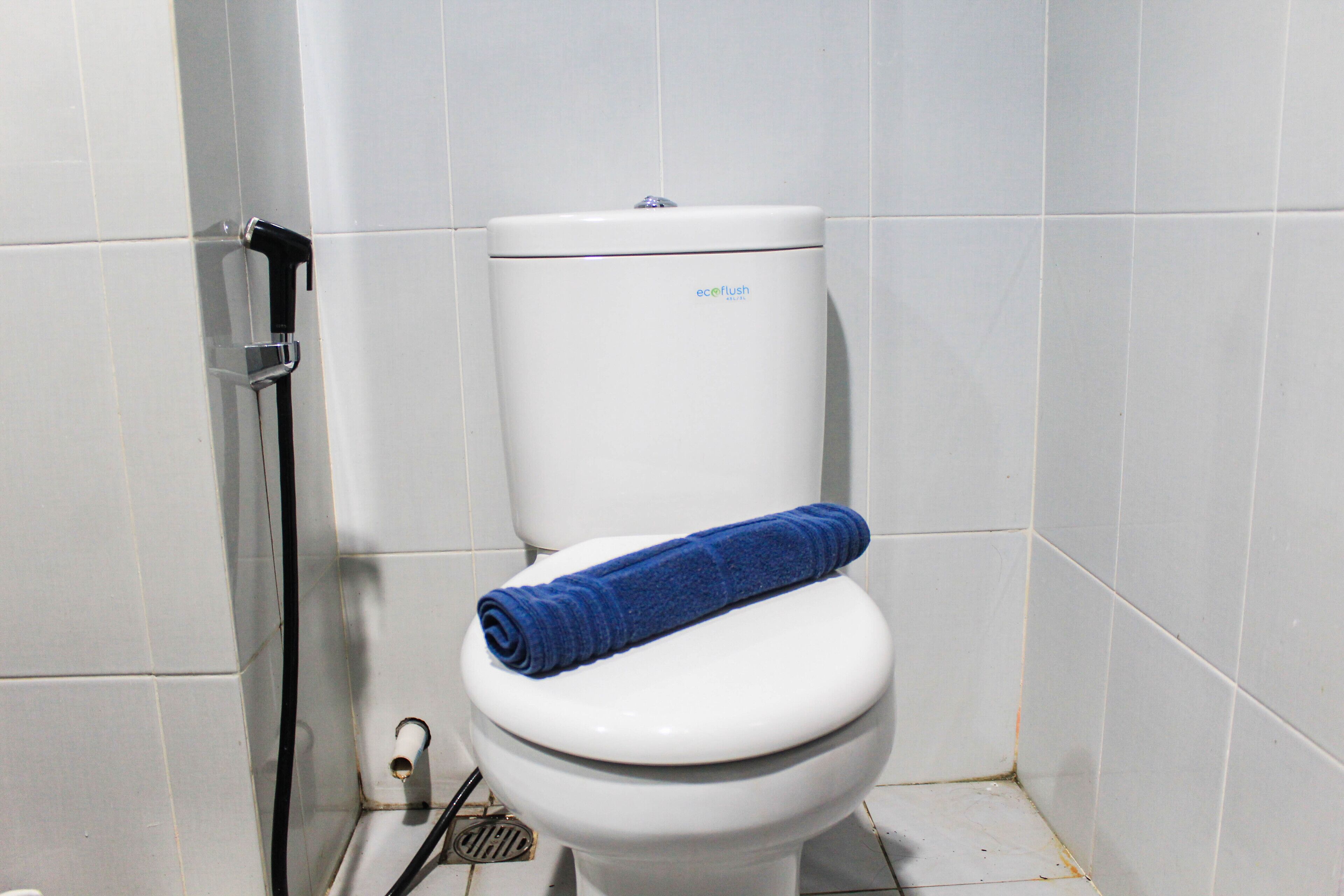 A white toilet with a blue towel on the seat and a toilet paper holder to the left.