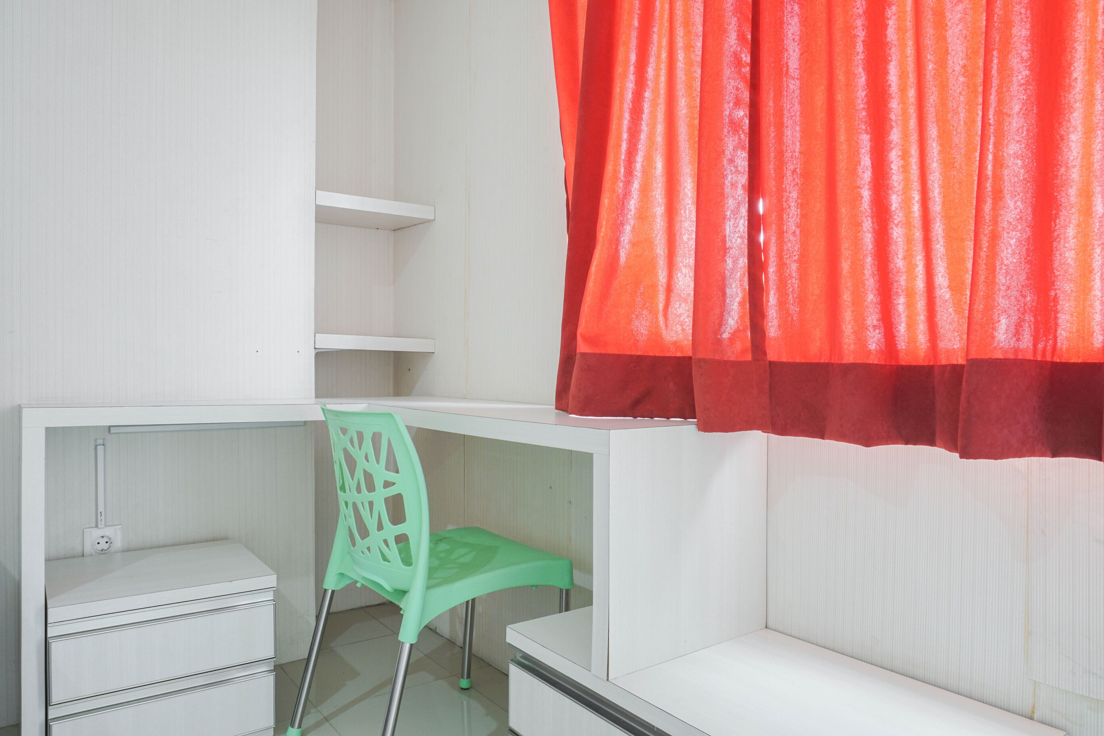 A white room with a desk, a green chair, and a red curtain.