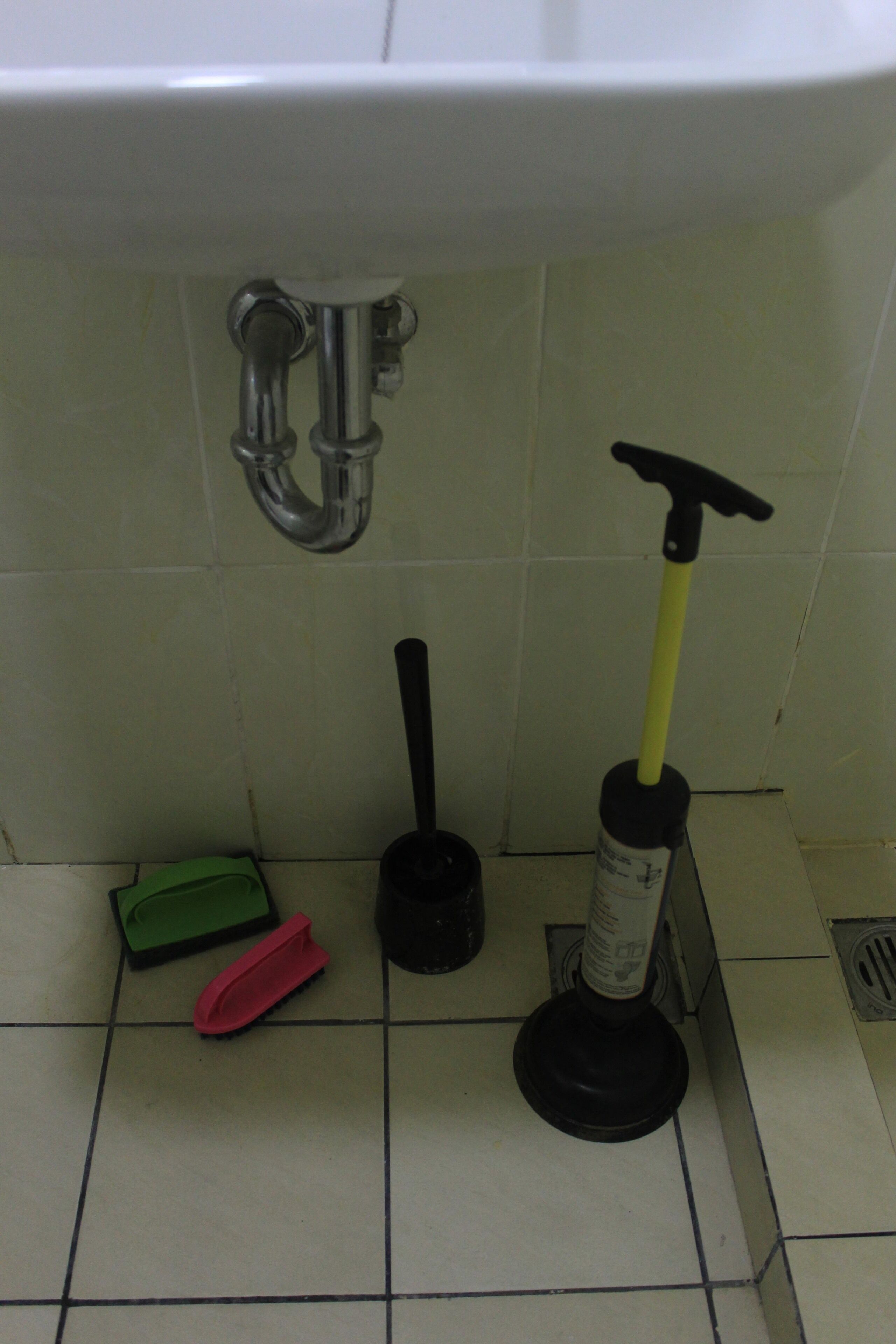 Un lavabo con grifo, un desatascador, un cepillo de limpieza y un paño de limpieza verde.