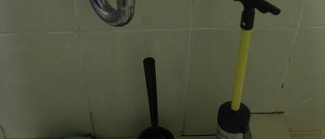 Un lavabo con grifo, un desatascador, un cepillo de limpieza y un paño de limpieza verde.