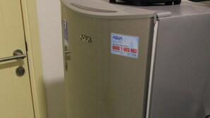 A compact refrigerator with a water dispenser, a door with a handle, and a label on the door. - Comfy Studio Apartment At M-Town Residence (Gading Serpong)
