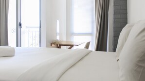 A hotel room with a bed, a desk, and a window with blinds. - Comfy Studio Apartment At M-Town Residence (Gading Serpong)