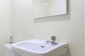 Une salle de bain avec un lavabo blanc, un miroir au-dessus et des toilettes à gauche.