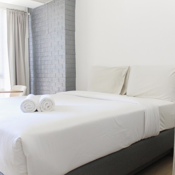 Une chambre d’hôtel moderne avec un grand lit, un mur en briques grises et une fenêtre avec des rideaux.