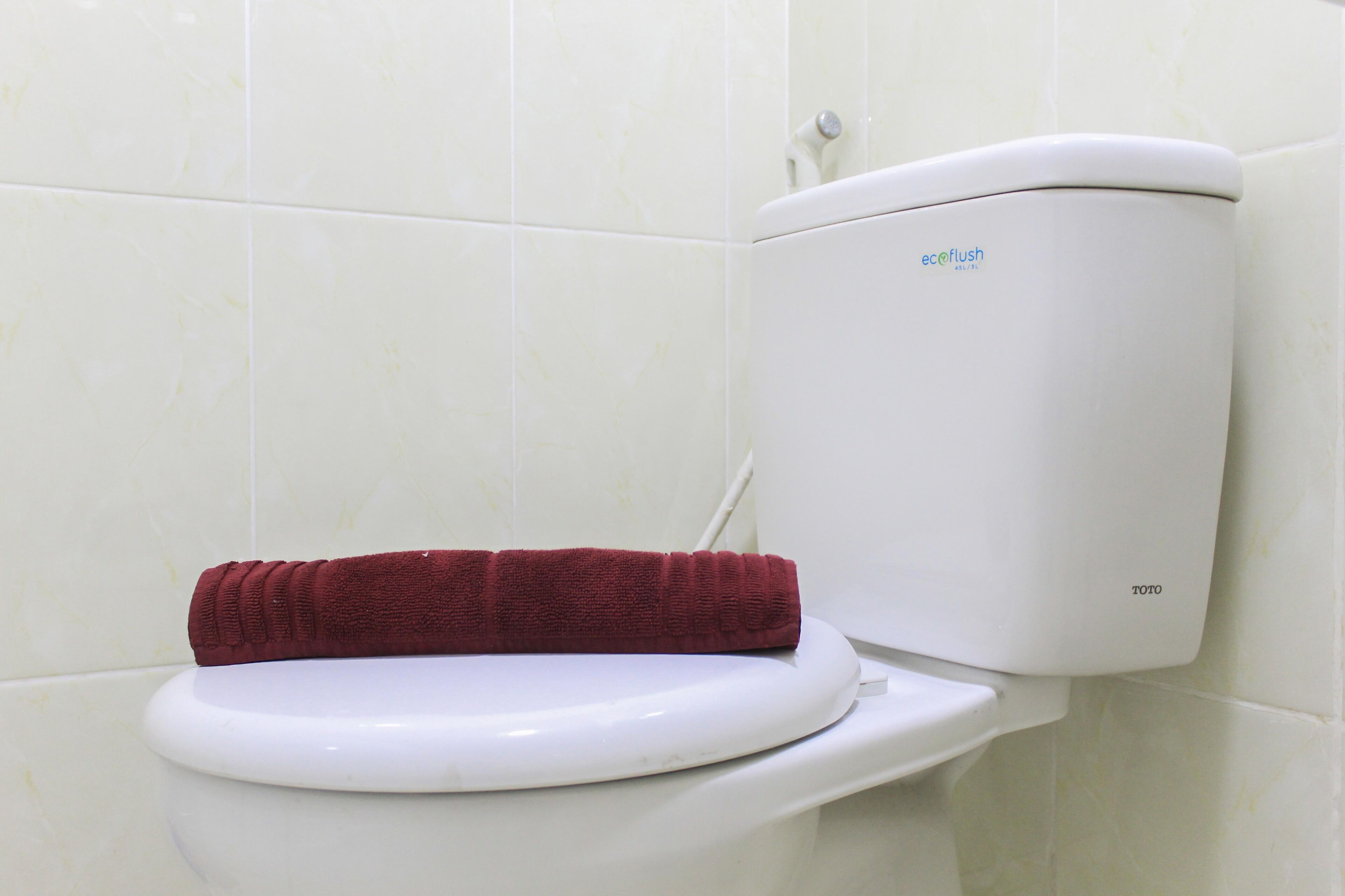 Eine Toilette mit weißem Sitz und Tank, sowie ein rotes Handtuch auf dem Sitz.