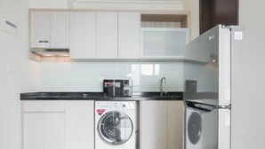 A compact kitchen with white cabinetry, a built-in washer and dryer, a refrigerator, and a microwave.