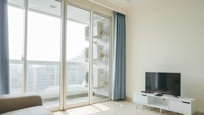 A modern living room with a sofa, a TV on a white cabinet, and a sliding glass door leading to a balcony.