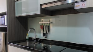 A modern kitchen with stainless steel appliances, a black countertop, and utensils hanging on the wall. - Nice And Fancy Studio Room At Menteng Park Apartment (Jakarta)
