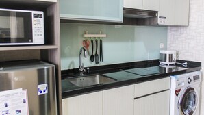 A compact kitchen with a stainless steel refrigerator, a microwave, a sink, and a washing machine. - Nice And Fancy Studio Room At Menteng Park Apartment (Jakarta)