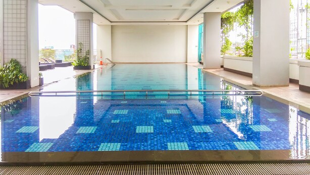 A large indoor swimming pool with clear blue tiles, surrounded by white walls and columns, with a view of greenery outside. - Comfortable And Nice Studio Room Apartement At H Residence (Jakarta)