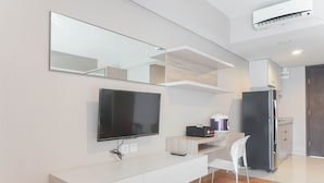 A modern, minimalist living room with a flat-screen TV, white console, and a compact kitchen area. - Comfortable And Nice Studio Room Apartement At H Residence (Jakarta)