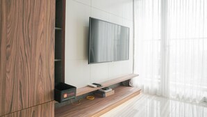 Ein modernes Wohnzimmer mit einem Flachbildfernseher an einer weißen Wand, darunter Holzregale und eine Glastür zu einem hellen Raum.