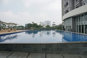 Una piscina moderna con borde de azulejos, rodeada por un deck de piedra y un muro cortina de vidrio.