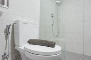 Un baño moderno con inodoro, cabina de ducha de vidrio y una toalla sobre el asiento del inodoro.