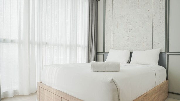 Ein modernes Schlafzimmer mit einem Bettgestell aus Holz, weißer Bettwäsche und durchscheinenden Vorhängen.