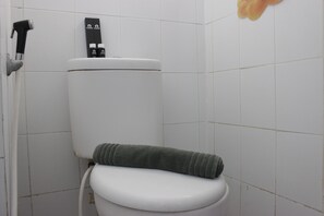Eine weiße Toilette mit einem grünen Handtuch auf dem Sitz und einem schwarzen Toilettenpapierhalter an der Wand.