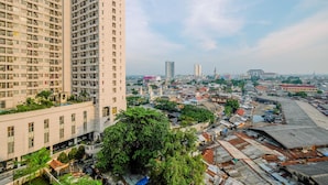A high-rise building with multiple floors and balconies, surrounded by a densely packed urban area with various buildings and a clear sky. - Warm And Cozy Studio Apartment At Margonda Residence 5 (Depok)