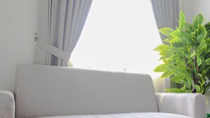 A white sofa in a room with a window and a potted plant. - Cozy Living Studio Room At Urbantown Serpong Apartment (South Tangerang)