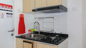 A compact kitchen with a gas stove, stainless steel sink, and wooden cabinets. - Cozy Living Studio Room At Urbantown Serpong Apartment (South Tangerang)