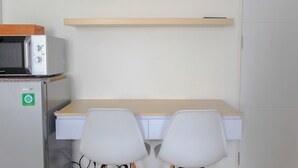 A compact kitchenette with a microwave, a refrigerator, and a wooden shelf above a desk with two chairs. - Cozy Living Studio Room At Urbantown Serpong Apartment (South Tangerang)