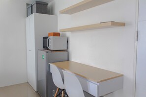 A compact kitchenette with a refrigerator, microwave, and a small wooden table.
