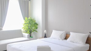 A modern hotel room with a wooden bed, white bedding, a potted plant, and a view of the outdoors through the window. - Cozy Living Studio Room At Urbantown Serpong Apartment (South Tangerang)