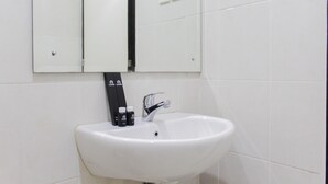 A white bathroom sink with a mirror above it and two electrical outlets on the wall. - Fresh And Bright Studio Room At Nifarro Park Apartment (Jakarta)
