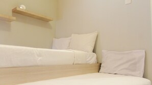 A single bed with white bedding and a wooden headboard, a bedside table, and a wall-mounted shelf with a clock. - Fresh And Bright Studio Room At Nifarro Park Apartment (Jakarta)
