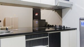 A kitchen with a black countertop, white cabinets, a stainless steel sink, and a built-in stove. - Fresh And Bright Studio Room At Nifarro Park Apartment (Jakarta)