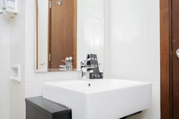 Une salle de bain avec un lavabo blanc, un miroir et une porte en bois.