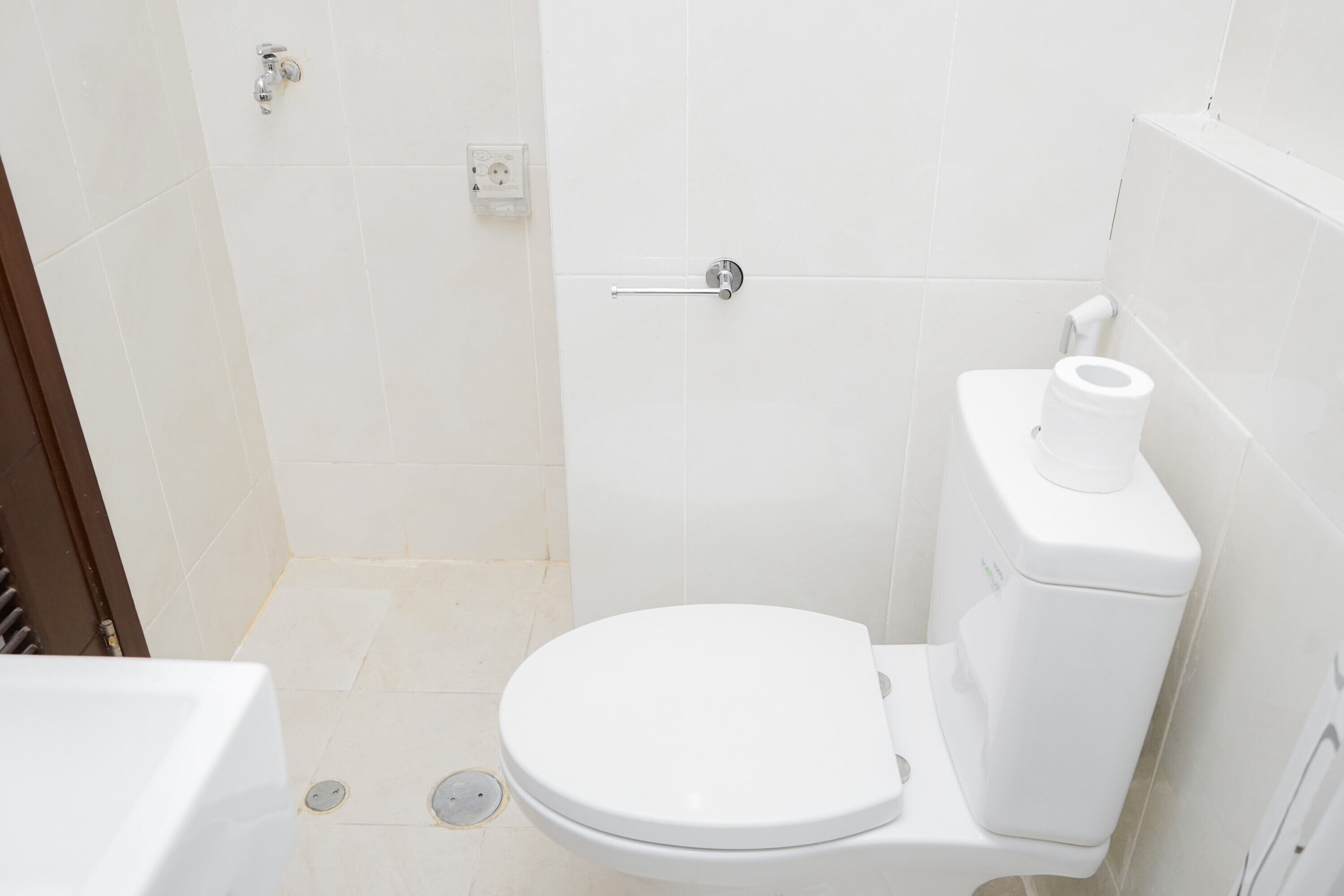Eine weiße Toilette mit Papierhandtuchhalter, Spülhebel und Wandfluschtaste.