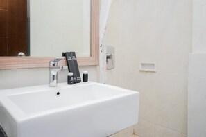 A white bathroom sink with a mirror above it, a faucet, and a soap dispenser on the wall.