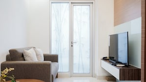 A modern living room with a sofa, a coffee table with a vase, a flat-screen TV on a wooden stand, and a sliding glass door with a bamboo pattern.